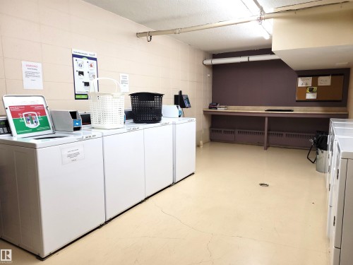Convenient laundry room featuring multiple washing machines, a long countertop, and ample floor space - 804 9028 Jasper Avenue, Edmonton, AB - Indoor Photo Showing Laundry Room
