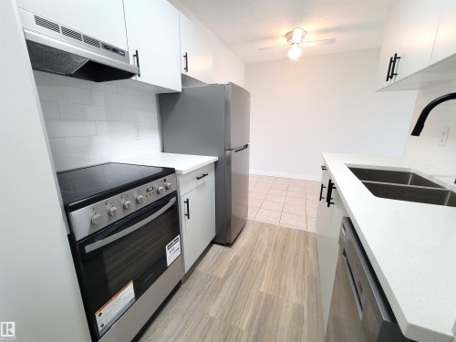 The kitchen features white cabinetry with black hardware, new stainless steel appliances including a refrigerator, stove, and dishwasher - still under warranty, and quartz countertops - 804 9028 Jasper Avenue, Edmonton, AB - Indoor Photo Showing Kitchen With Double Sink
