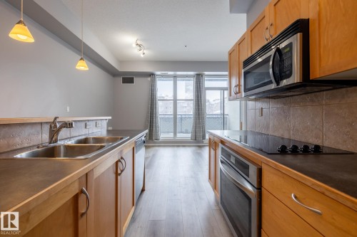 The kitchen features light wood cabinetry, stainless steel appliances, a double basin sink, and pendant lighting - 210 10147 112 Street, Edmonton, AB - Indoor Photo Showing Kitchen With Double Sink