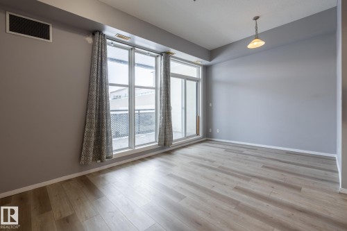 The interior features light-toned flooring, light gray walls, and large windows that provide natural light - 210 10147 112 Street, Edmonton, AB - Indoor Photo Showing Other Room