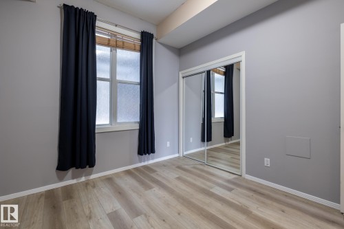 This room features light wood-style flooring, a window with blinds, and mirrored sliding closet doors - 210 10147 112 Street, Edmonton, AB - Indoor Photo Showing Other Room