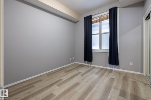 This room features light-toned wood flooring and a window dressed with dark curtains and blinds - 210 10147 112 Street, Edmonton, AB - Indoor Photo Showing Other Room