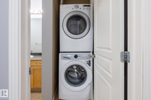 Convenient laundry area featuring a stacked washer and dryer, with a bathroom visible beyond - 210 10147 112 Street, Edmonton, AB - Indoor Photo Showing Laundry Room