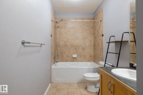 The bathroom features a bathtub with a tiled shower surround, a toilet, and a vanity with a sink - 210 10147 112 Street, Edmonton, AB - Indoor Photo Showing Bathroom