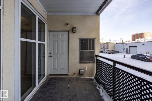 The property features a private outdoor patio with stamped concrete flooring, a solid exterior door, and a grilled window - 210 10147 112 Street, Edmonton, AB - Outdoor With Exterior