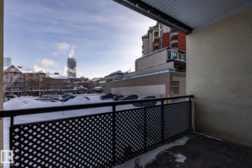 The property includes a private balcony with a black metal lattice railing, offering views of the surrounding urban landscape and distant high-rise buildings - 210 10147 112 Street, Edmonton, AB - Outdoor