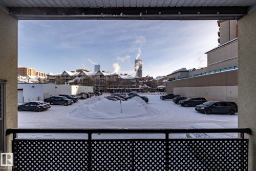 The property offers a balcony with a geometric patterned railing, providing views of the surrounding urban landscape and a parking area with vehicles - 210 10147 112 Street, Edmonton, AB - Outdoor