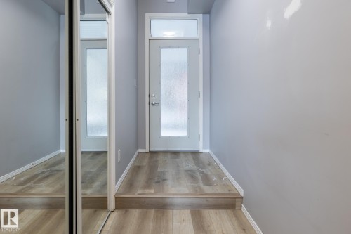 The entry features light-colored wood flooring, a white door with a frosted glass panel, and a mirrored closet door - 210 10147 112 Street, Edmonton, AB - Indoor Photo Showing Other Room