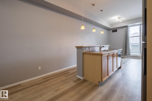 Open concept living space featuring light wood-look flooring, a kitchen island with integrated sink, and pendant lighting - 210 10147 112 Street, Edmonton, AB - Indoor Photo Showing Kitchen