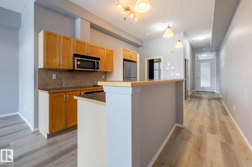 The kitchen features light wood cabinetry, a stainless steel microwave, and a black cooktop - 210 10147 112 Street, Edmonton, AB - Indoor Photo Showing Kitchen