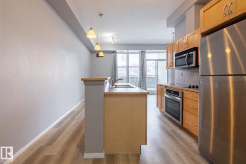 Well-appointed kitchen featuring wood cabinetry, stainless steel appliances, and a kitchen island with a sink - 210 10147 112 Street, Edmonton, AB - Indoor Photo Showing Kitchen With Stainless Steel Kitchen With Double Sink