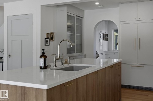 The kitchen features a spacious island with a light-colored countertop and a stainless steel sink, complemented by light wood-toned base cabinetry with brass hardware - 9228 100 Avenue, Edmonton, AB - Indoor Photo Showing Kitchen With Upgraded Kitchen