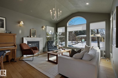 Living area featuring hardwood floors, a stone fireplace, and an arched window - 9228 100 Avenue, Edmonton, AB - Indoor Photo Showing Living Room With Fireplace