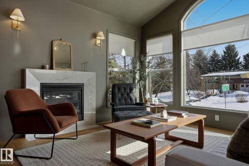 Living room featuring a fireplace with a marble-look surround, hardwood floors, and large windows providing natural light - 9228 100 Avenue, Edmonton, AB - Indoor Photo Showing Living Room With Fireplace