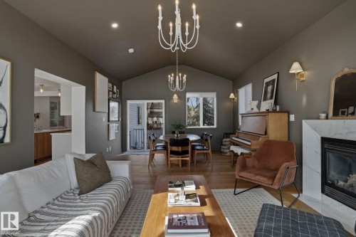 The living area features vaulted ceilings with recessed lighting and two chandeliers, hardwood flooring, and a fireplace with a white marble surround - 9228 100 Avenue, Edmonton, AB - Indoor Photo Showing Living Room With Fireplace
