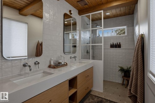 This bathroom features a double vanity with integrated sinks and wall-mounted faucets, set against a tiled wall - 9228 100 Avenue, Edmonton, AB - Indoor Photo Showing Bathroom