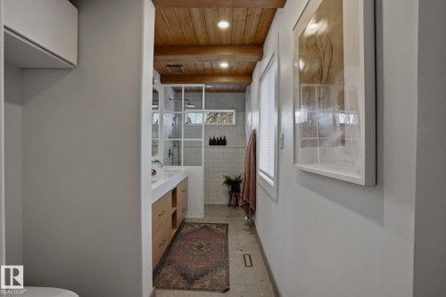 The bathroom features a double vanity with wooden cabinetry, a wood-beamed ceiling with recessed lighting, and a walk-in shower with a grid-patterned glass partition - 9228 100 Avenue, Edmonton, AB - Indoor