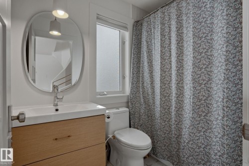 This bathroom features a contemporary vanity with a basin sink, an oval mirror, and an adjacent toilet - 9228 100 Avenue, Edmonton, AB - Indoor Photo Showing Bathroom