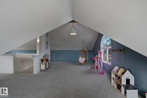 A spacious attic space featuring sloped ceilings, carpet flooring, a window providing natural light, and a ceiling light fixture - 9228 100 Avenue, Edmonton, AB - 