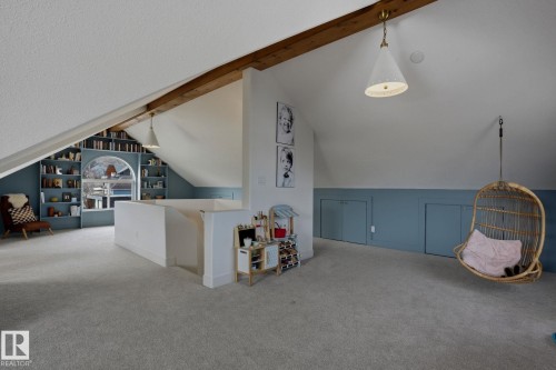 This versatile attic space features sloped ceilings, light-colored carpeting, and a built-in bookshelf surrounding a window - 9228 100 Avenue, Edmonton, AB - Indoor Photo Showing Other Room