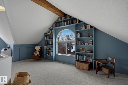 This versatile attic space features sloped ceilings, built-in shelving, an arched window, and a visible wooden beam - 9228 100 Avenue, Edmonton, AB - Indoor