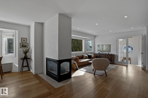 Living room featuring hardwood flooring, a corner fireplace with a black surround, recessed lighting, and bay windows - 9228 100 Avenue, Edmonton, AB - Indoor Photo Showing Living Room With Fireplace