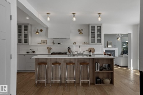 The kitchen features hardwood floors, a large island with seating, white countertops, and white cabinetry - 9228 100 Avenue, Edmonton, AB - Indoor Photo Showing Kitchen