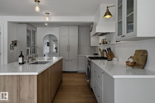 The kitchen features white countertops, wood flooring, and a kitchen island with a sink and faucet - 9228 100 Avenue, Edmonton, AB - Indoor Photo Showing Kitchen With Upgraded Kitchen