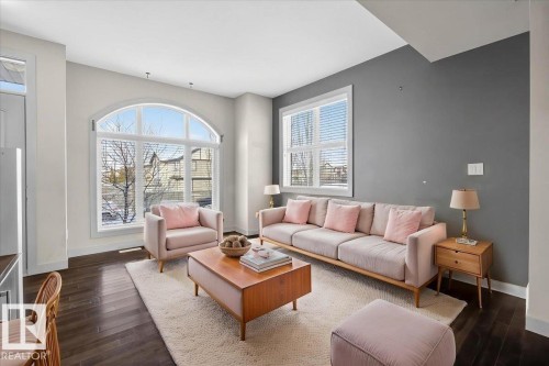 The living area features dark wood flooring, a large arched window, and a secondary rectangular window, providing ample natural light - 2105 Casselman Link Link, Edmonton, AB - Indoor Photo Showing Living Room