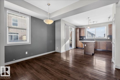 Open concept living area featuring dark hardwood floors, a kitchen with brown cabinetry, light countertops, and a central island - 2105 Casselman Link Link, Edmonton, AB - Indoor Photo Showing Kitchen