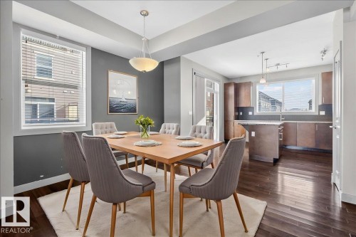 This property features an open dining area with dark hardwood floors and a contemporary light fixture - 2105 Casselman Link Link, Edmonton, AB - Indoor Photo Showing Dining Room