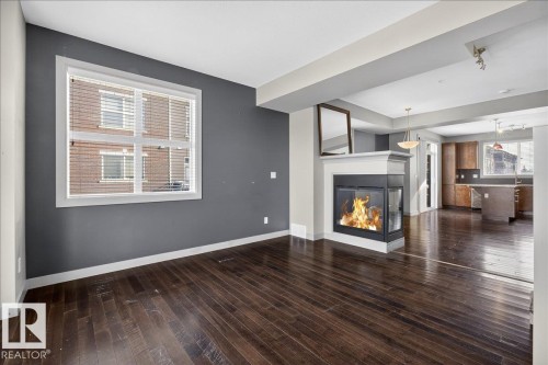 Living area with dark hardwood floors, a corner fireplace, and a large window - 2105 Casselman Link Link, Edmonton, AB - Indoor With Fireplace