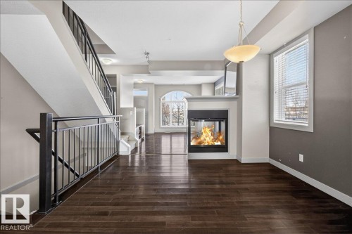 Expansive open concept living area featuring dark hardwood floors, a contemporary fireplace, and a large arched window providing natural light - 2105 Casselman Link Link, Edmonton, AB - Indoor Photo Showing Other Room With Fireplace