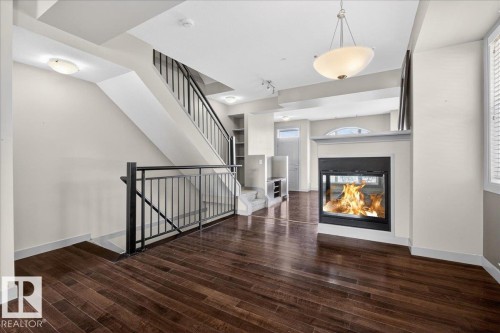 The living area features rich hardwood flooring, a modern fireplace with a white mantel, and a stylish pendant light fixture - 2105 Casselman Link Link, Edmonton, AB - Indoor With Fireplace
