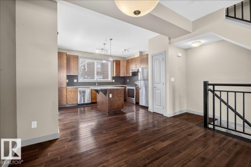 Open-concept kitchen and living area featuring dark wood flooring, light-colored walls, and contemporary light fixtures - 2105 Casselman Link Link, Edmonton, AB - Indoor Photo Showing Kitchen