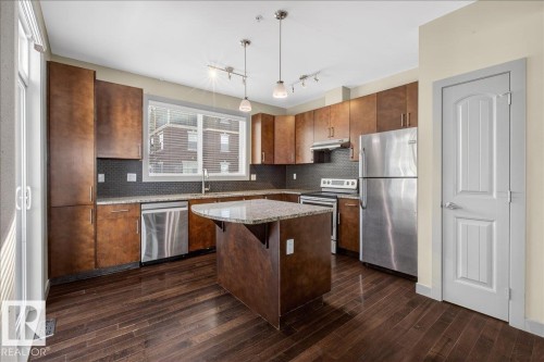 The kitchen features dark wood cabinetry, stainless steel appliances, and a central island with a granite countertop - 2105 Casselman Link Link, Edmonton, AB - Indoor Photo Showing Kitchen With Stainless Steel Kitchen
