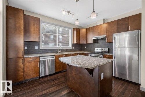 The kitchen features dark wood cabinetry, stainless steel appliances, granite countertops, and a central island - 2105 Casselman Link Link, Edmonton, AB - Indoor Photo Showing Kitchen With Stainless Steel Kitchen With Upgraded Kitchen