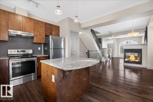 The open-concept living space features dark hardwood floors and a fireplace - 2105 Casselman Link Link, Edmonton, AB - Indoor Photo Showing Kitchen With Stainless Steel Kitchen With Upgraded Kitchen