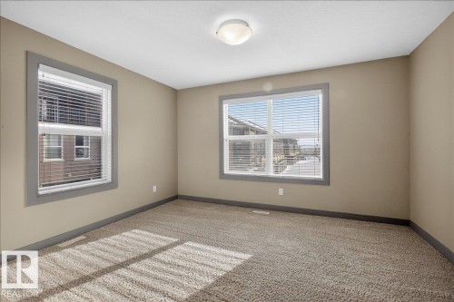 This room features carpeted flooring and neutral-toned walls, complemented by two windows fitted with blinds - 2105 Casselman Link Link, Edmonton, AB - Indoor Photo Showing Other Room