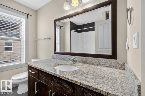 Bathroom featuring a dark wood vanity with a granite countertop, an undermount sink, and a framed mirror - 2105 Casselman Link Link, Edmonton, AB - Indoor Photo Showing Bathroom
