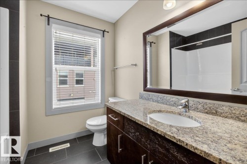 Bathroom featuring a vanity with a granite countertop, a toilet, a window with blinds, and dark floor tiles - 2105 Casselman Link Link, Edmonton, AB - Indoor Photo Showing Bathroom