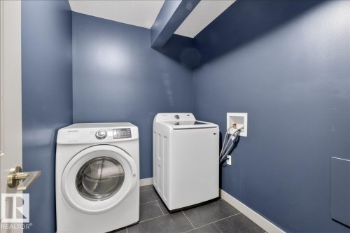 Laundry area featuring a front-loading washing machine, a top-loading washing machine, and dark floor tiles - 2105 Casselman Link Link, Edmonton, AB - Indoor Photo Showing Laundry Room