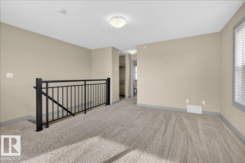 This versatile loft area features light-colored carpeting, neutral painted walls, and a black metal railing - 2105 Casselman Link Link, Edmonton, AB - Indoor Photo Showing Other Room