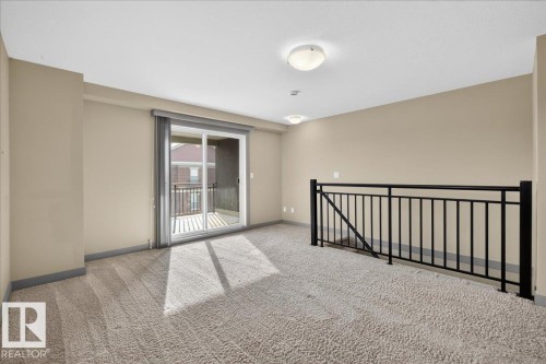 This open area features carpeted flooring, a sliding glass door providing access to a balcony, and a black metal railing - 2105 Casselman Link Link, Edmonton, AB - Indoor Photo Showing Other Room