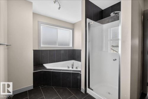 This bathroom features a corner soaking tub with dark tile surround, a separate shower with a clear glass door, and a window providing natural light - 2105 Casselman Link Link, Edmonton, AB - Indoor Photo Showing Bathroom