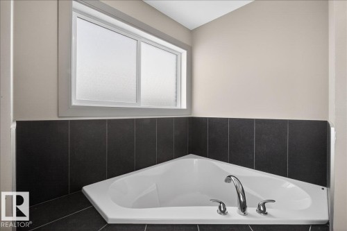 Corner soaking tub with chrome fixtures, surrounded by dark tiled walls and a frosted window - 2105 Casselman Link Link, Edmonton, AB - Indoor Photo Showing Bathroom