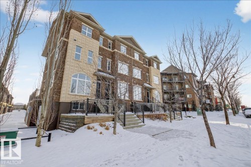 The property features a multi-story exterior with a combination of brick and stone cladding, multiple windows, and a paved walkway leading to the entrance - 2105 Casselman Link Link, Edmonton, AB - Outdoor With Facade