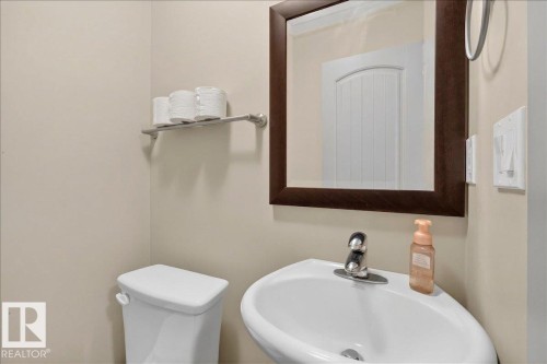Bathroom featuring a white toilet, a corner sink with a chrome faucet, and a mirror with a dark wood frame - 2105 Casselman Link Link, Edmonton, AB - Indoor Photo Showing Bathroom