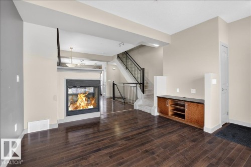 This inviting living area features dark hardwood flooring, a modern fireplace with a black frame, and neutral-toned walls - 2105 Casselman Link Link, Edmonton, AB - Indoor With Fireplace