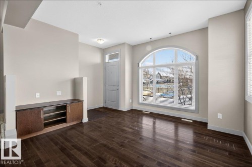 Inviting entry area featuring rich hardwood floors, an arched window with blinds, and a built-in media console with dark countertops - 2105 Casselman Link Link, Edmonton, AB - Indoor Photo Showing Other Room